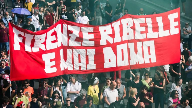 Foto von Demo mit Banner "Firenze ribelle e mai doma", laut Bildunterschrift im Artikel übersetzbar als "Rebellisches Florenz, niemals gebändigt".  