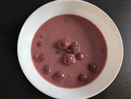 A photo of a bowl filled with a thick pink colored soup and cherries