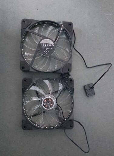 2 shitty case fans. The same model, but one of them is kept upside down. Sticker reads: B.J 12025 FAN 650-2000RPM\DC 12V 0.37A, followed by various safety/certification symbols, the part no., then RGB MADE IN CHINA. The connectors are MOLEX 8981 (the fat ones which connect to PSU outlets), with only 2 pins used. They have foam pads at the corners. The only redeemable quality is that the coil covering part is transparent and can be used for "educational" purposes.