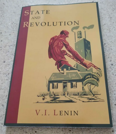 Copy of Vladimir Lenin's "State and Revolution". The book features a gray-green trim surrounding a dark gold cover with a maroon bar near the spine. "V. I. LENIN" is on the bottom of the cover. "STATE AND REVOLUTION" is at the top of the cover. The imager depicts a shirtless, muscular man wearing gloves, a cap, and overalls as he holds what appears to be some kind of soldering device in his hands. A small cottage is below him while a large factory tower stands behind him.