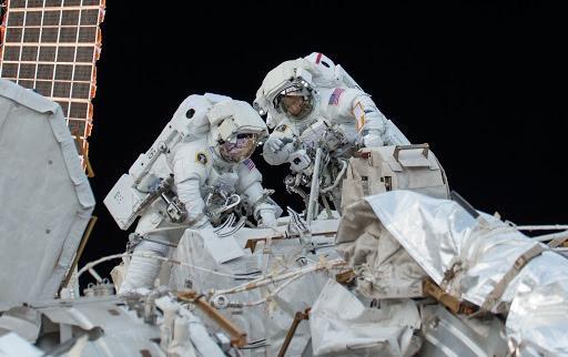 Two astronauts conduct an EVA on a large equipment