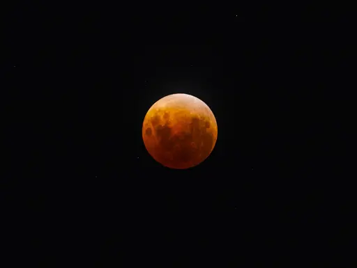 A full moon, tinted in orange and red, during the peak of the eclipse.  Stars are visible in the background of the night sky