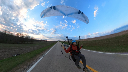 Powered Paraglider flying down a road with farm fields on either side, rural