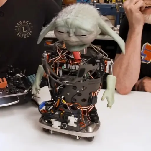 Grogu animatronic with green flesh head and arms but robotic skeleton everywhere else. Grogu has his eyes closed and is looking downward forlornly