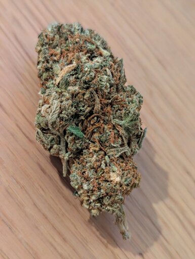Close-up photo of a Lemon Haze bud resting on a wooden table. It’s a compact, frosty nug with bright orange hairs and a mix of light and dark green tones